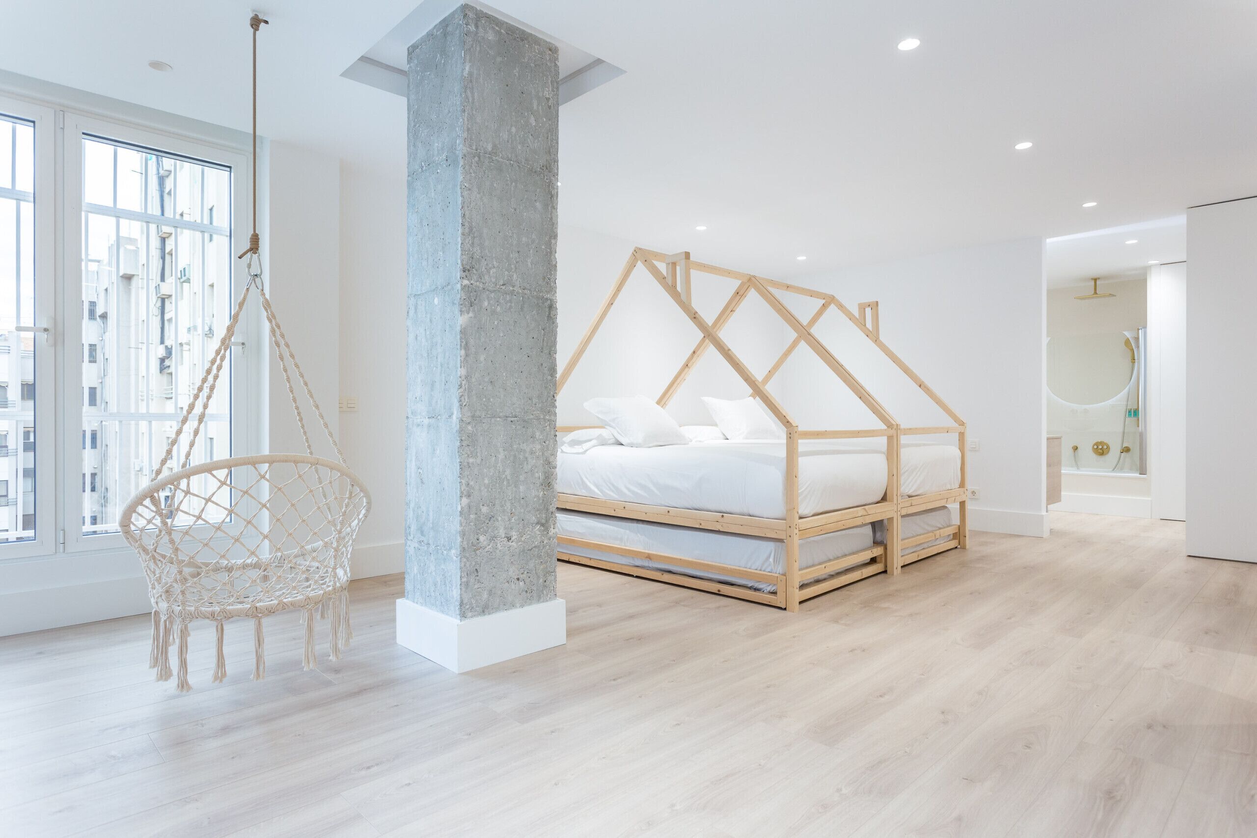 A modern bedroom with a wooden bed frame, a hanging chair, and a concrete pillar.