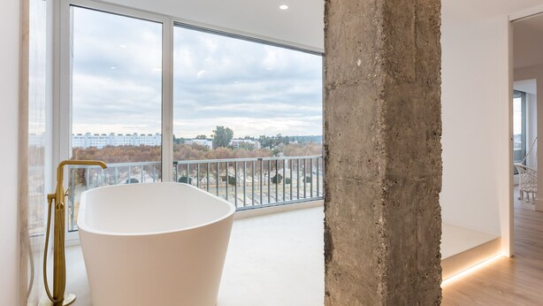 Ein modernes Badezimmer mit freistehender Badewanne, großen Fenstern und einer Betonstütze.