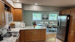 Una cocina moderna con armarios de madera, encimeras de granito, un refrigerador de acero inoxidable y una zona de comedor con una mesa y sillas.
