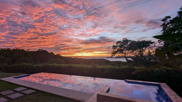 A swimming pool with a view of a sunset over water and hills. - A place to relax and connect with nature (Playa iguanita)