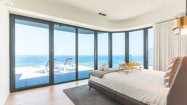 A modern bedroom with a large bed, a view of the ocean, and a balcony with outdoor furniture. - Majestic Penthouse View by Atlantic Holiday (Funchal)