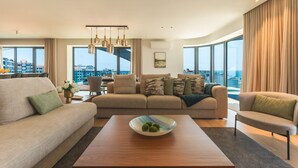 A modern living room with a sofa set, a coffee table with decorative items, and large windows offering a city view. - Majestic Penthouse View by Atlantic Holiday (Funchal)