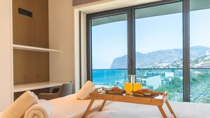 A hotel room with a bed, a tray with croissants and orange juice, and a view of the sea and buildings. - Majestic Penthouse View by Atlantic Holiday (Funchal)