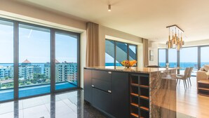A modern kitchen with a large island, a dining area, and large windows offering a city view. - Majestic Penthouse View by Atlantic Holiday (Funchal)