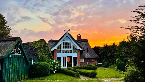 Una casa tradizionale con tetto di paglia, un sentiero in pietra e un giardino curato.