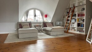 Una stanza in stile loft con soffitto alto, una grande finestra, una libreria, una scala a pioli e un televisore.