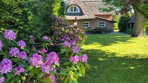 Una casa con tetto di paglia, un prato e un giardino con fiori rosa.
