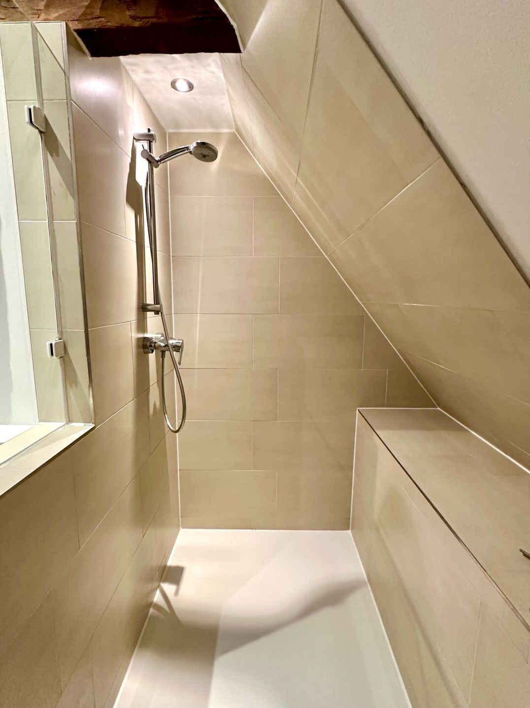 A small, modern shower with a handheld showerhead and a wall-mounted faucet.