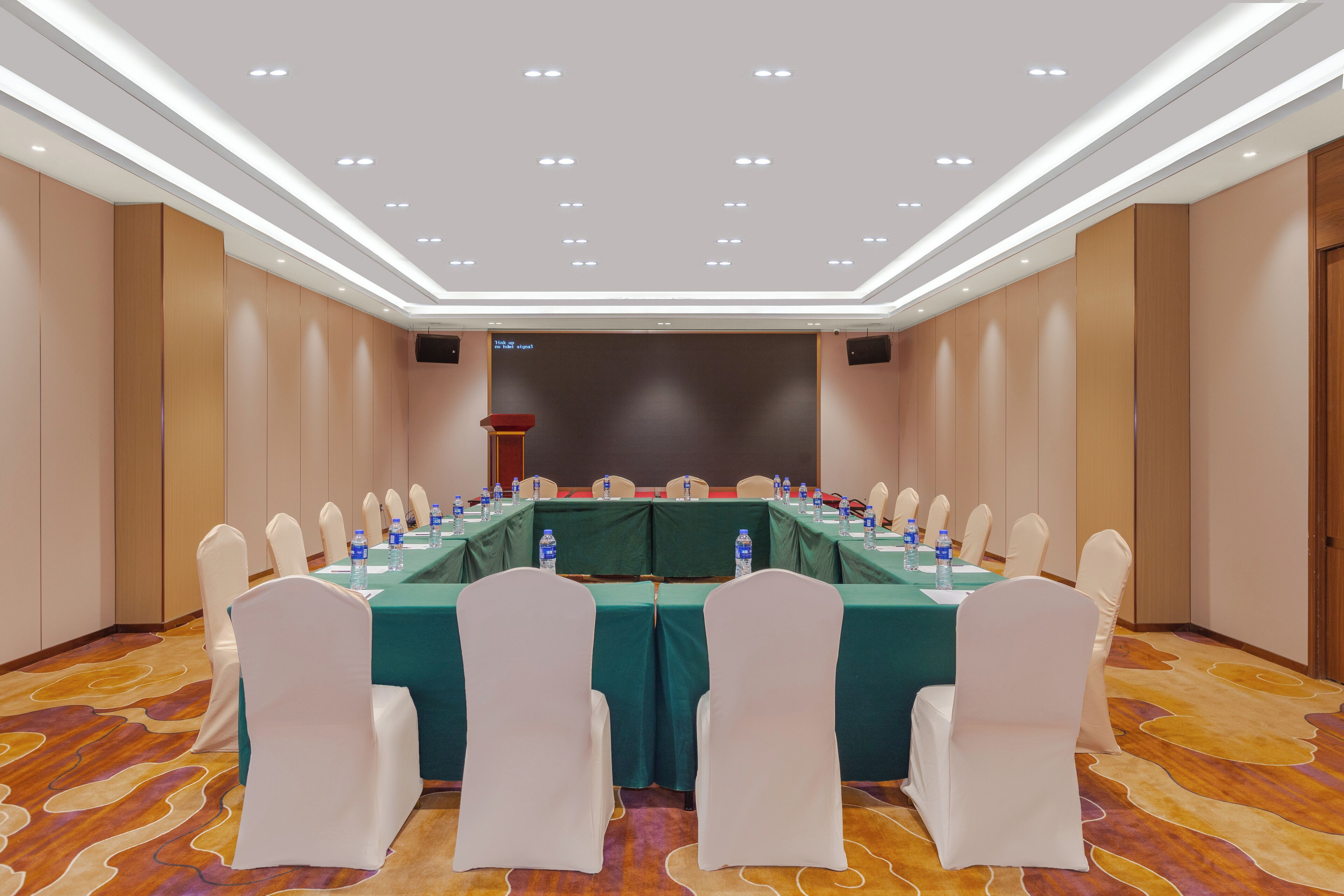 A conference room with a long table, white chairs, and a green tablecloth.