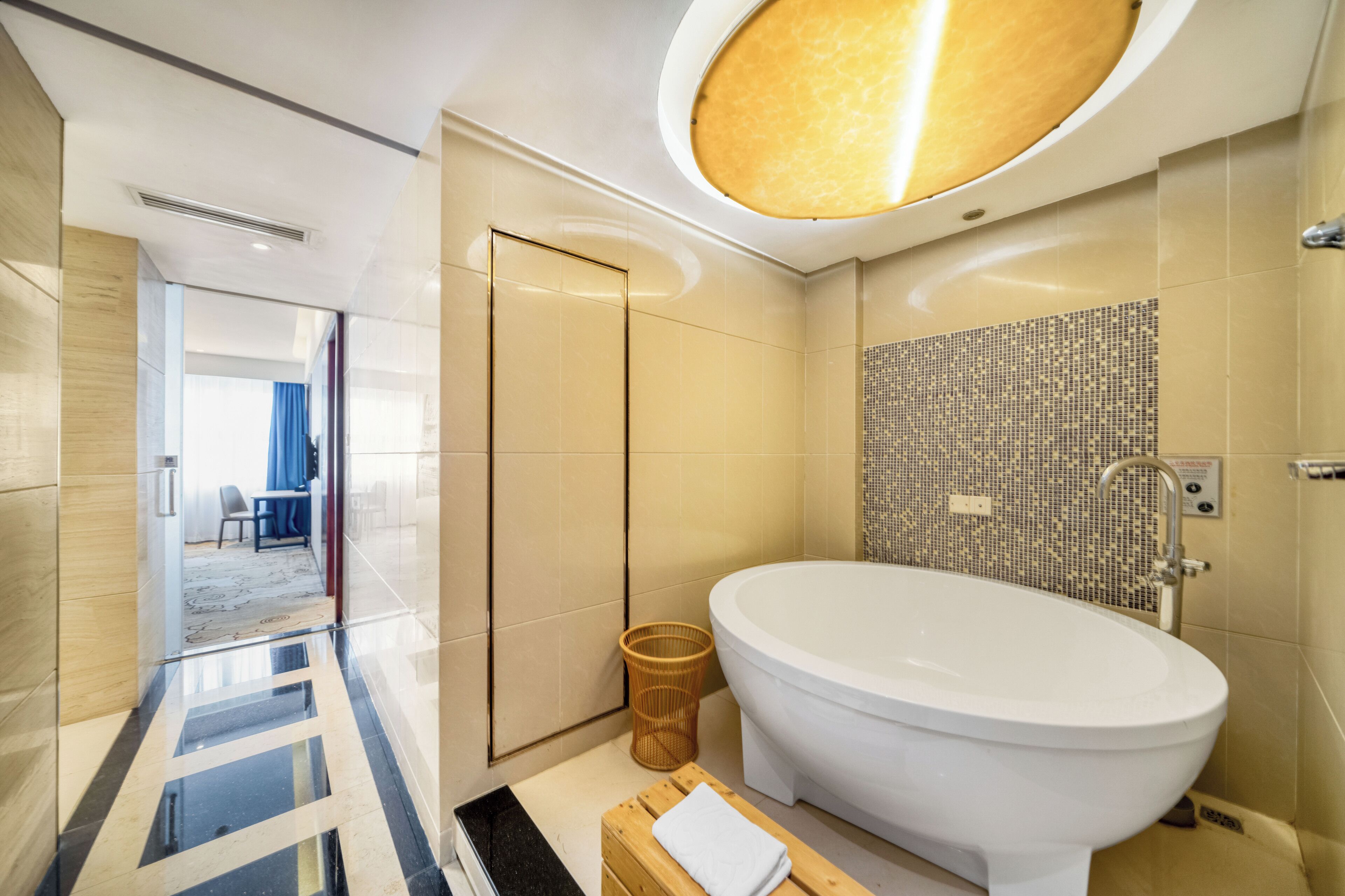 Un baño moderno con una bañera grande, un taburete pequeño de madera con una toalla y un revestimiento de pared con diseño de mosaico.