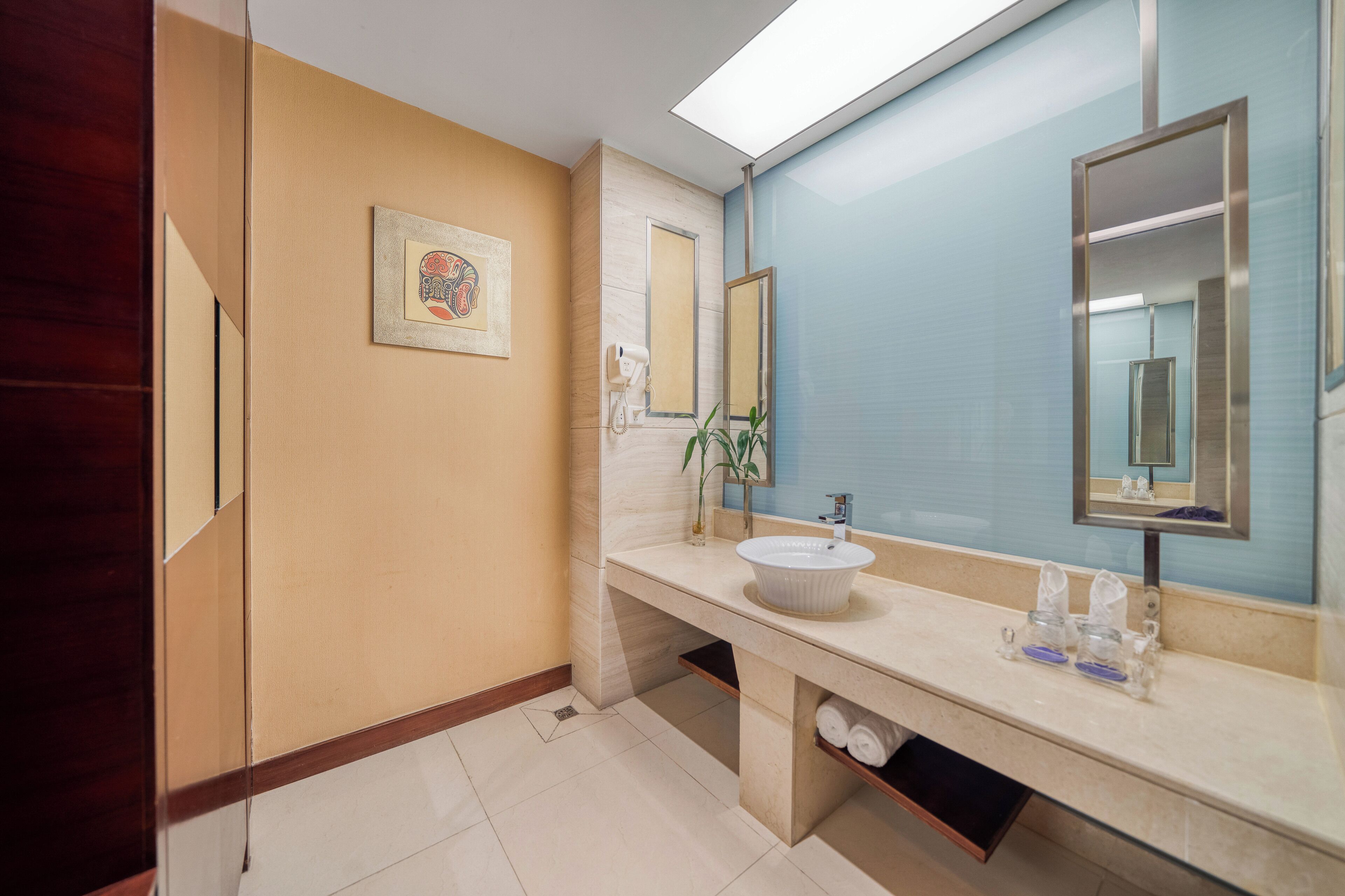 A modern bathroom with a beige vanity, a large mirror, and a framed artwork on the wall.