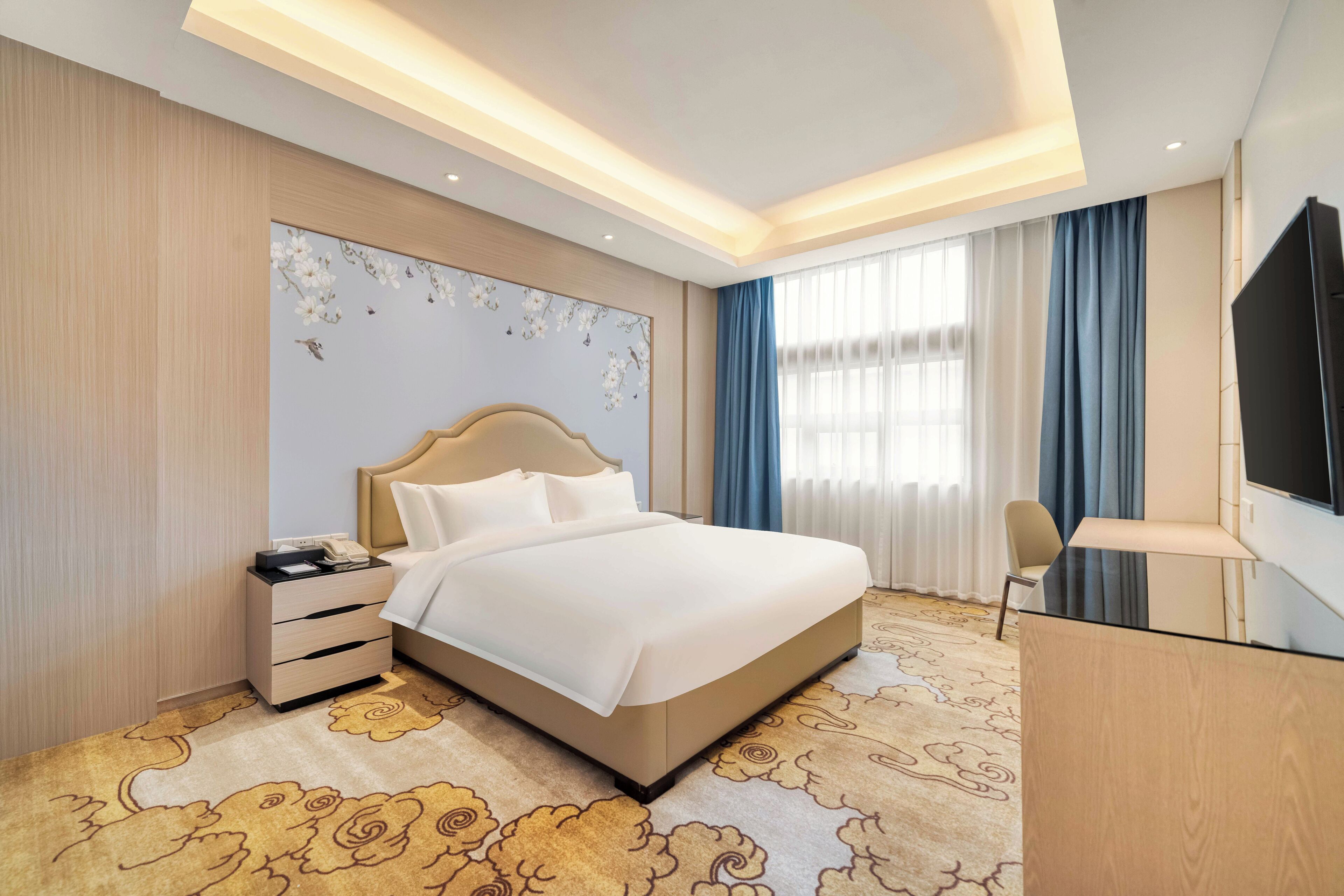 Habitación de hotel con una cama grande, un escritorio, una silla, un televisor y una mesita de noche con teléfono.