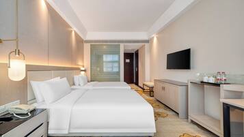 A hotel room with two beds, a desk, a chair, a TV, and a minibar.