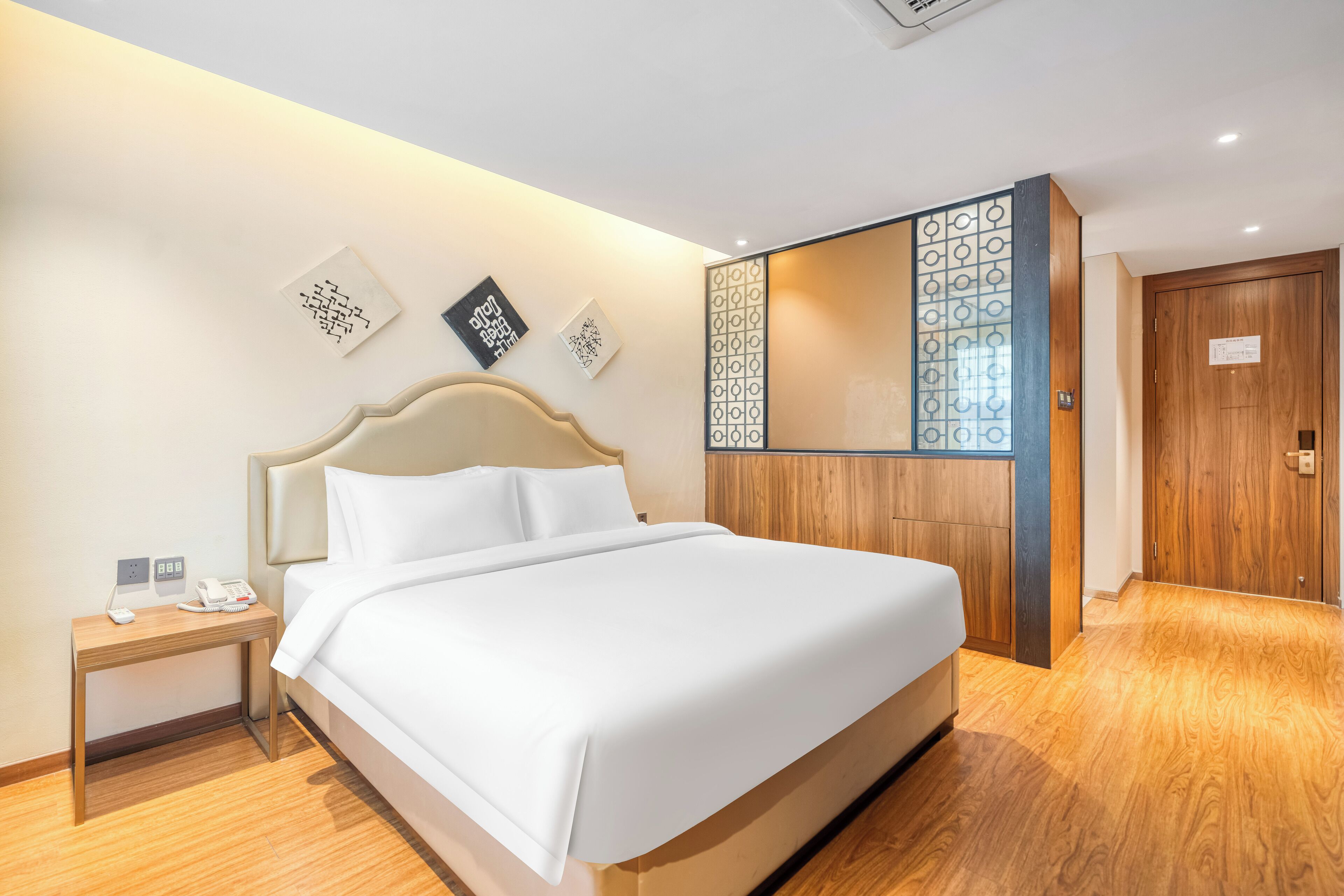 A hotel room with a large bed, a bedside table with a phone, and a wooden wardrobe.