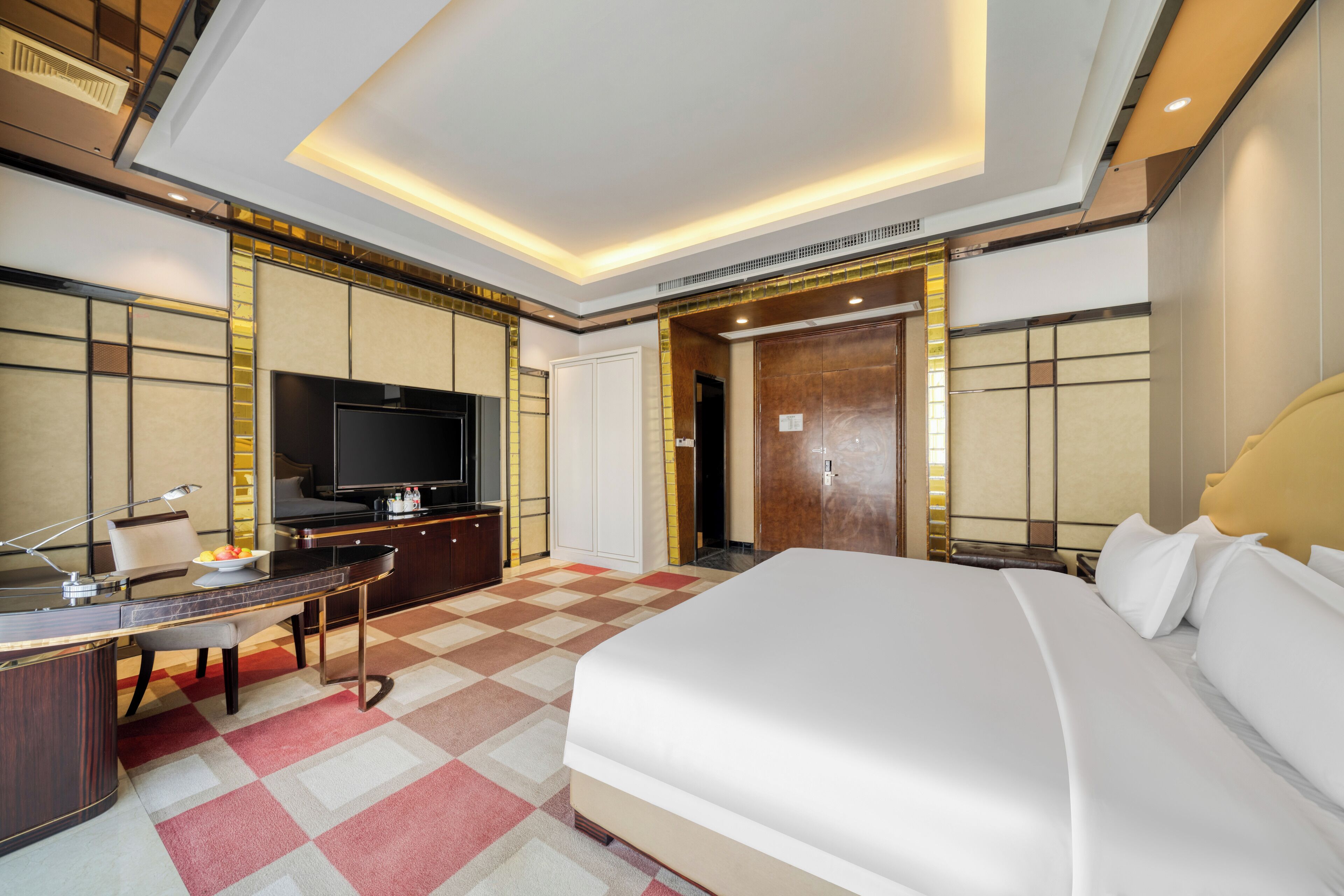 A modern hotel room with a large bed, a desk with a computer, a television, and a wardrobe.