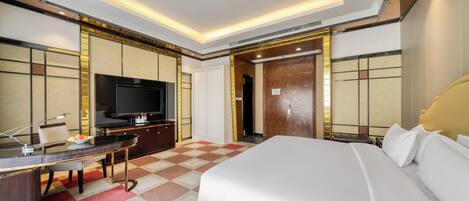 A modern hotel room with a large bed, a desk with a computer, a television, and a wardrobe.