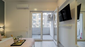 A hotel room with a bed, a bedside table with a bottle and glasses, a tray with food, a TV on the wall, and a sliding glass door to the balcony. - Central 4BR Flat - 2 Units Combined with Balconies, Near Cismigiu, 2 Kitchens & 2 Baths (Bucharest)