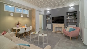 A modern living room with a sofa, a pink armchair, a dining table with chairs, a fireplace, and a TV mounted on the wall. - Central 4BR Flat - 2 Units Combined with Balconies, Near Cismigiu, 2 Kitchens & 2 Baths (Bucharest)