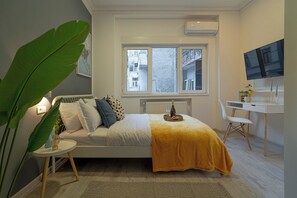 Een slaapkamer met een bed, een bureau, een stoel, een grote plant en een televisie.