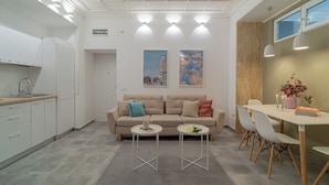 A modern kitchen with white cabinets and a built-in oven. There is a beige sofa with cushions, a small round table, and a dining table with chairs. - Central 4BR Flat - 2 Units Combined with Balconies, Near Cismigiu, 2 Kitchens & 2 Baths (Bucharest)