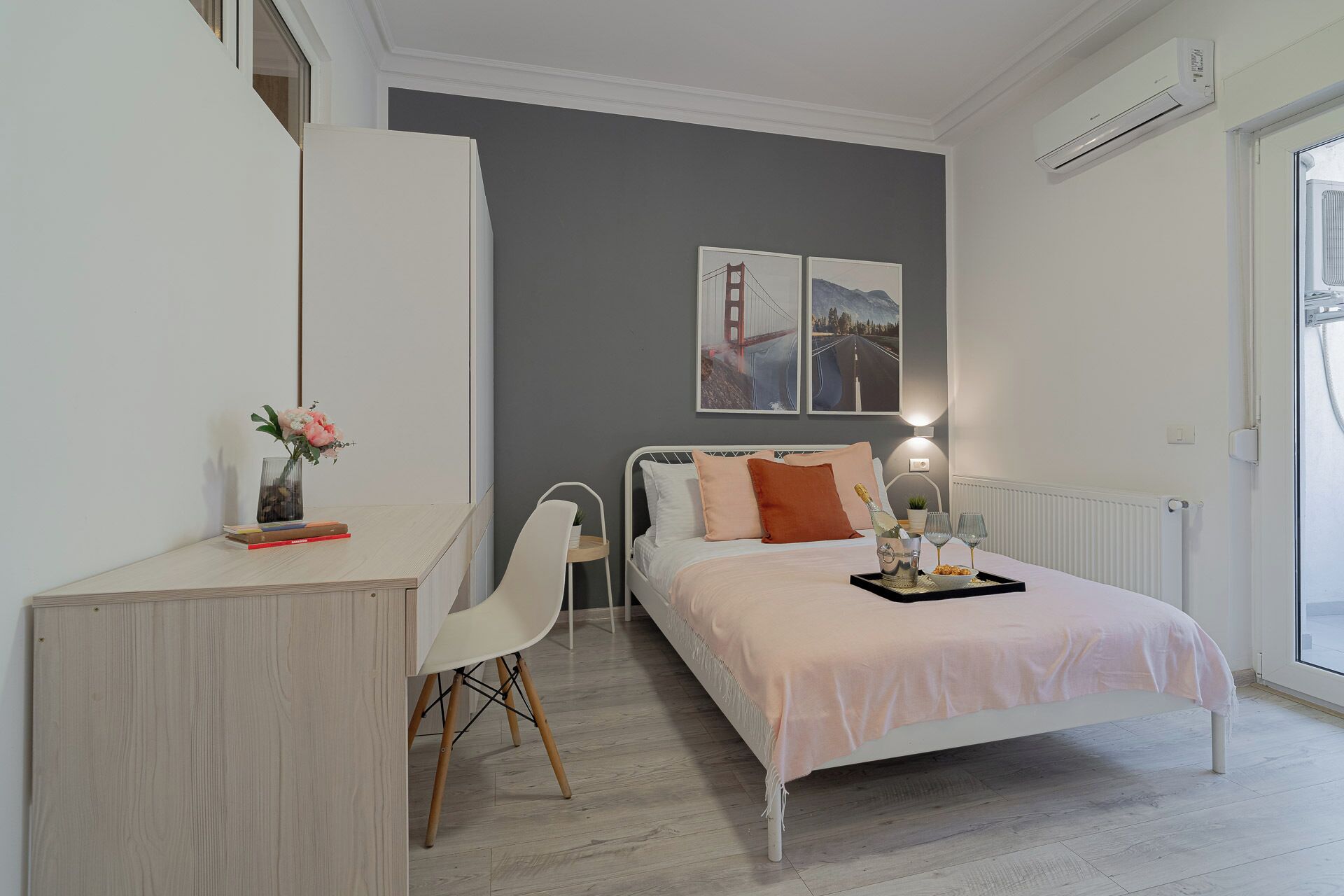Un dormitorio con cama, mesita de noche, silla y escritorio con un florero.