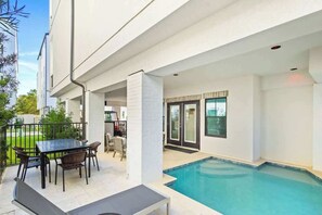 Un espace extérieur abrité comprenant une piscine, une table avec des chaises et une vue sur un bâtiment voisin.