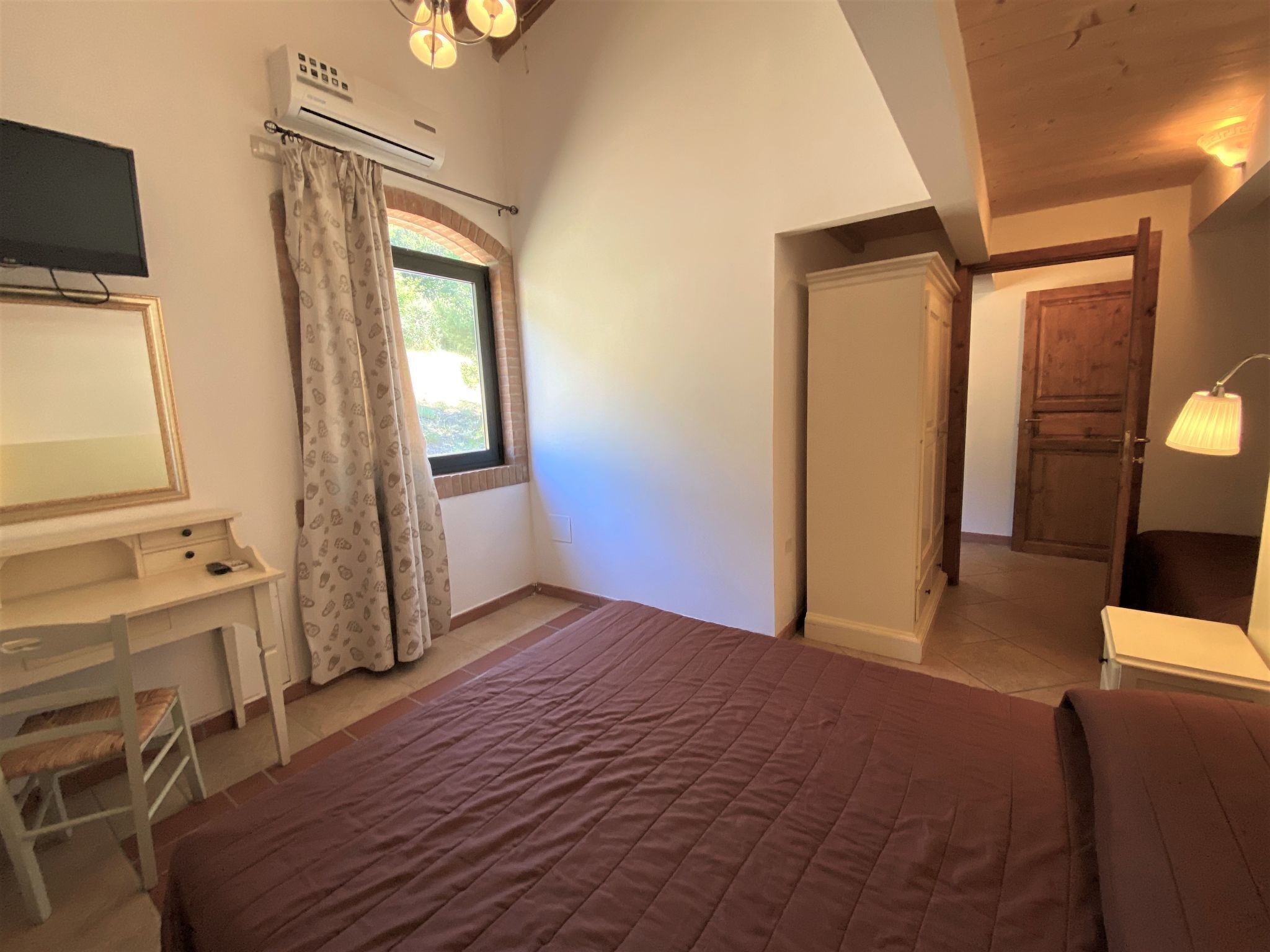 A bedroom with a bed, a desk, a television, and a window with curtains.