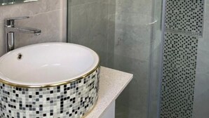 A bathroom with a round sink, a mirror, and a shower with a glass door. - Dash motel (Papakura)