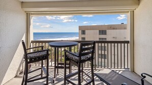 Un balcón con mesa y sillas, con vista a una playa y un edificio.