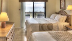 A hotel room with a bed, a nightstand, a lamp, a dresser, and a view of the sea through a balcony door. - Apartment Steps from the Beach! (Deerfield Beach)