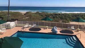 A pool with a view of the ocean and beach, surrounded by lounge chairs and umbrellas. - Apartment Steps from the Beach! (Deerfield Beach)