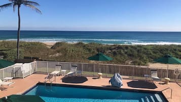 A pool with a view of the ocean and beach, surrounded by lounge chairs and umbrellas.