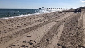 A beach with a pier extending into the water, sandy terrain, and footprints. - Apartment Steps from the Beach! (Deerfield Beach)