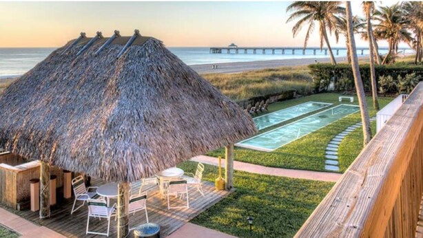 A thatched-roof outdoor seating area with a pool and a view of the beach and pier. - Apartment Steps from the Beach! (Deerfield Beach)