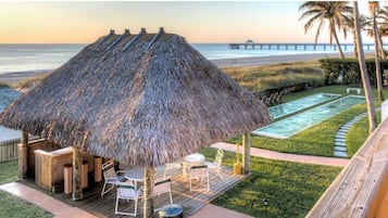 A thatched-roof outdoor seating area with a pool and a view of the beach and pier.