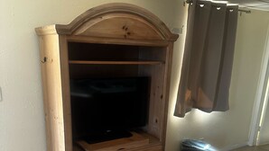 A wooden cabinet with a television, drawers, and a trash bin.