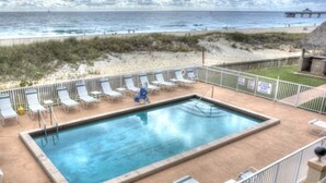 A rectangular pool with a metal ladder, surrounded by white lounge chairs and a metal fence.