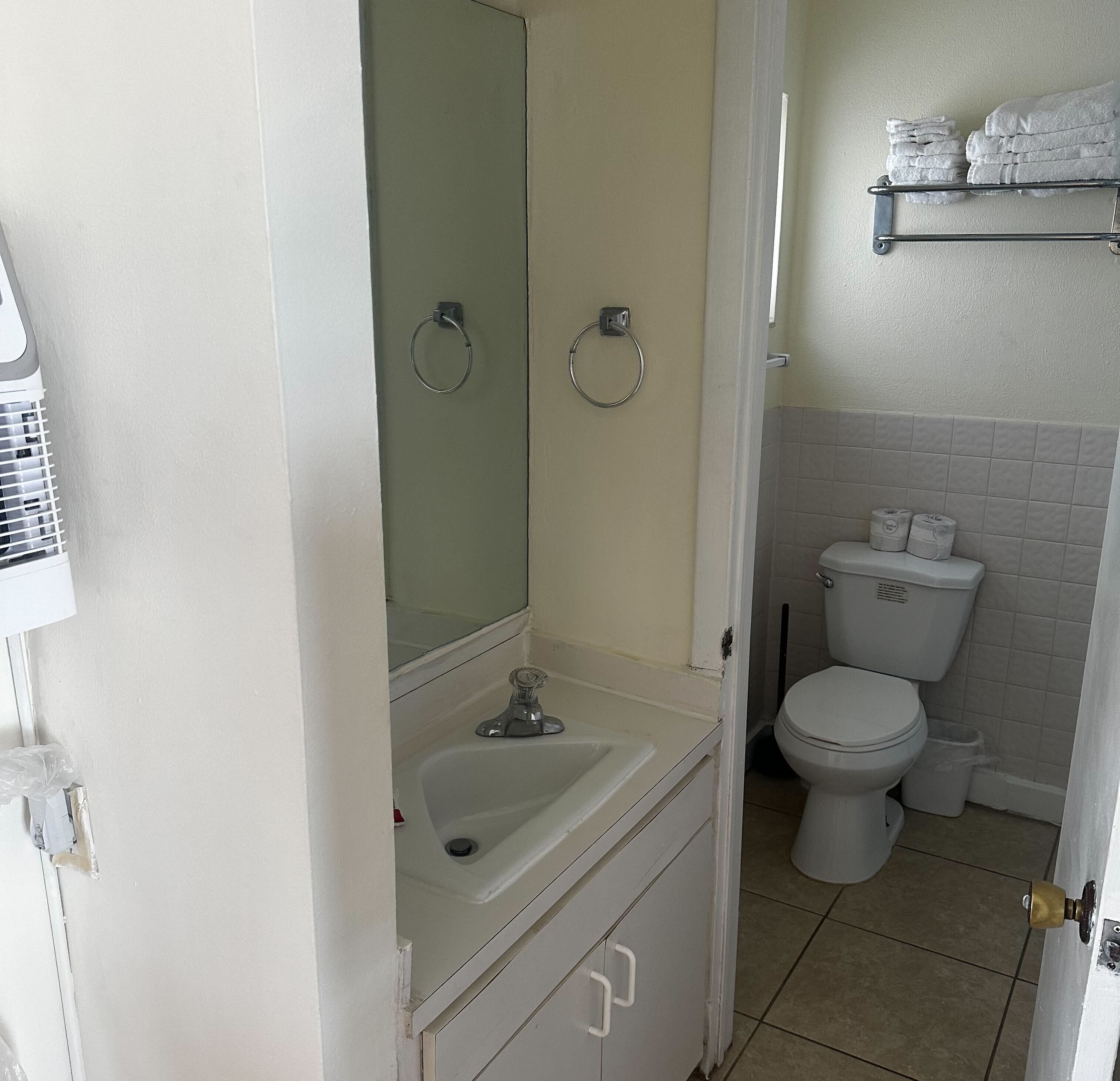 Een badkamer met een wit wastafel, toilet en een spiegel. Er zitten twee handdoekhouders aan de muur.
