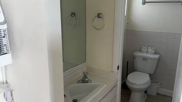Een badkamer met een wit wastafel, toilet en een spiegel. Er zitten twee handdoekhouders aan de muur.
