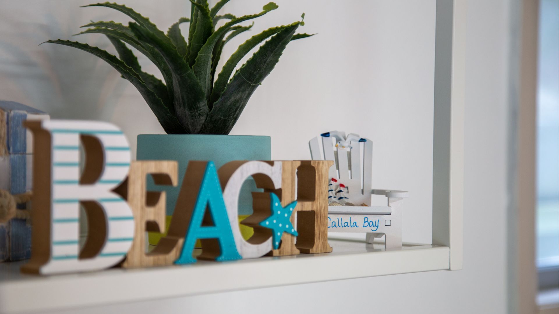 Une étagère avec des lettres en bois formant le mot « PLAGE » et une plante en pot.