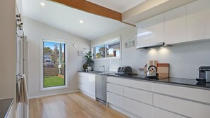 Una cocina moderna con armarios blancos, encimera negra y vista al jardín trasero a través de un ventanal corredero.
