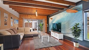 Una sala de estar moderna con techo de madera, televisor grande, sofá y comedor.