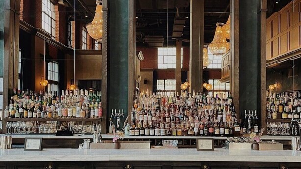 Un bar avec un long comptoir, de nombreux tabourets et une grande variété de bouteilles et de verres.