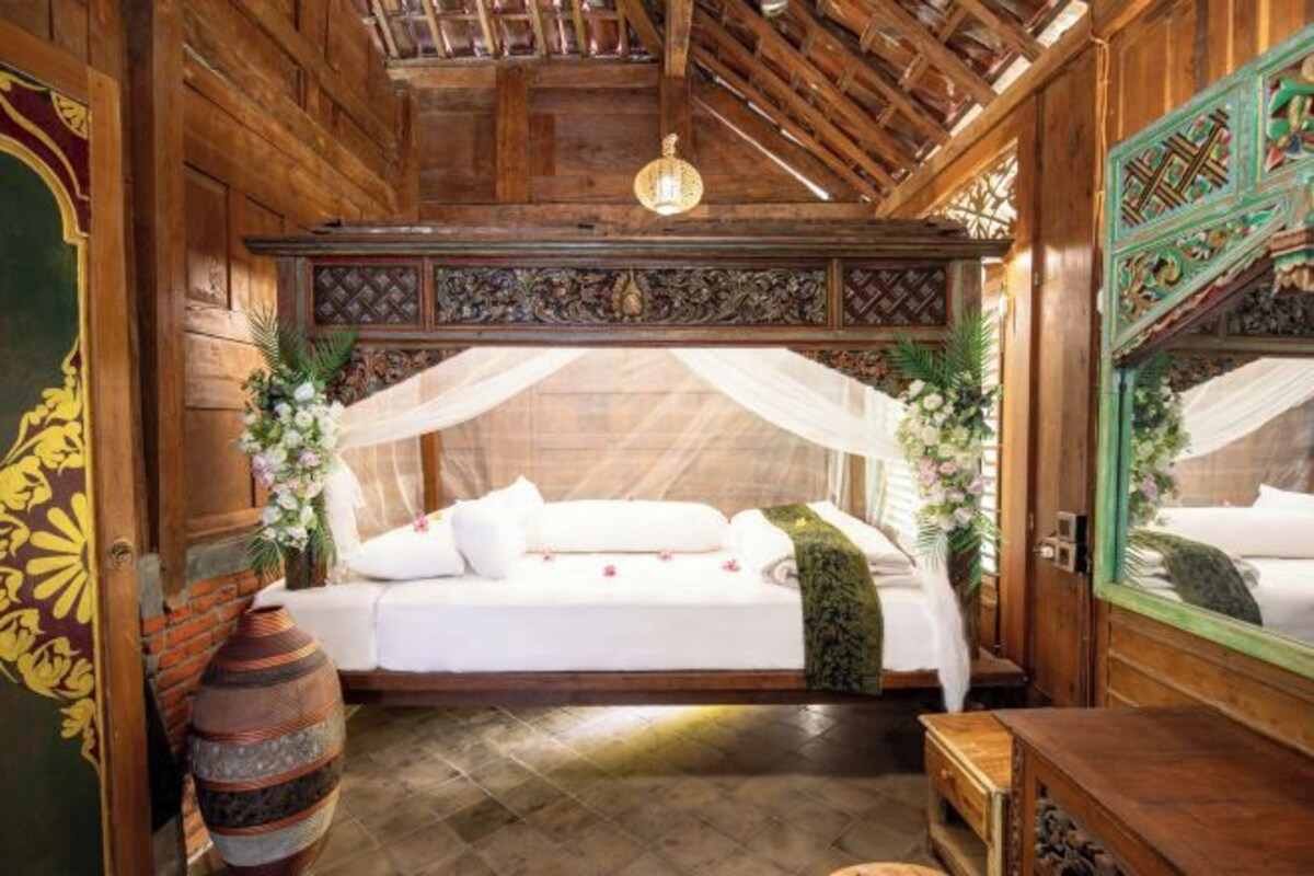 Ein Zimmer aus Holz mit einem Bett, einem Spiegel und einer Vase.