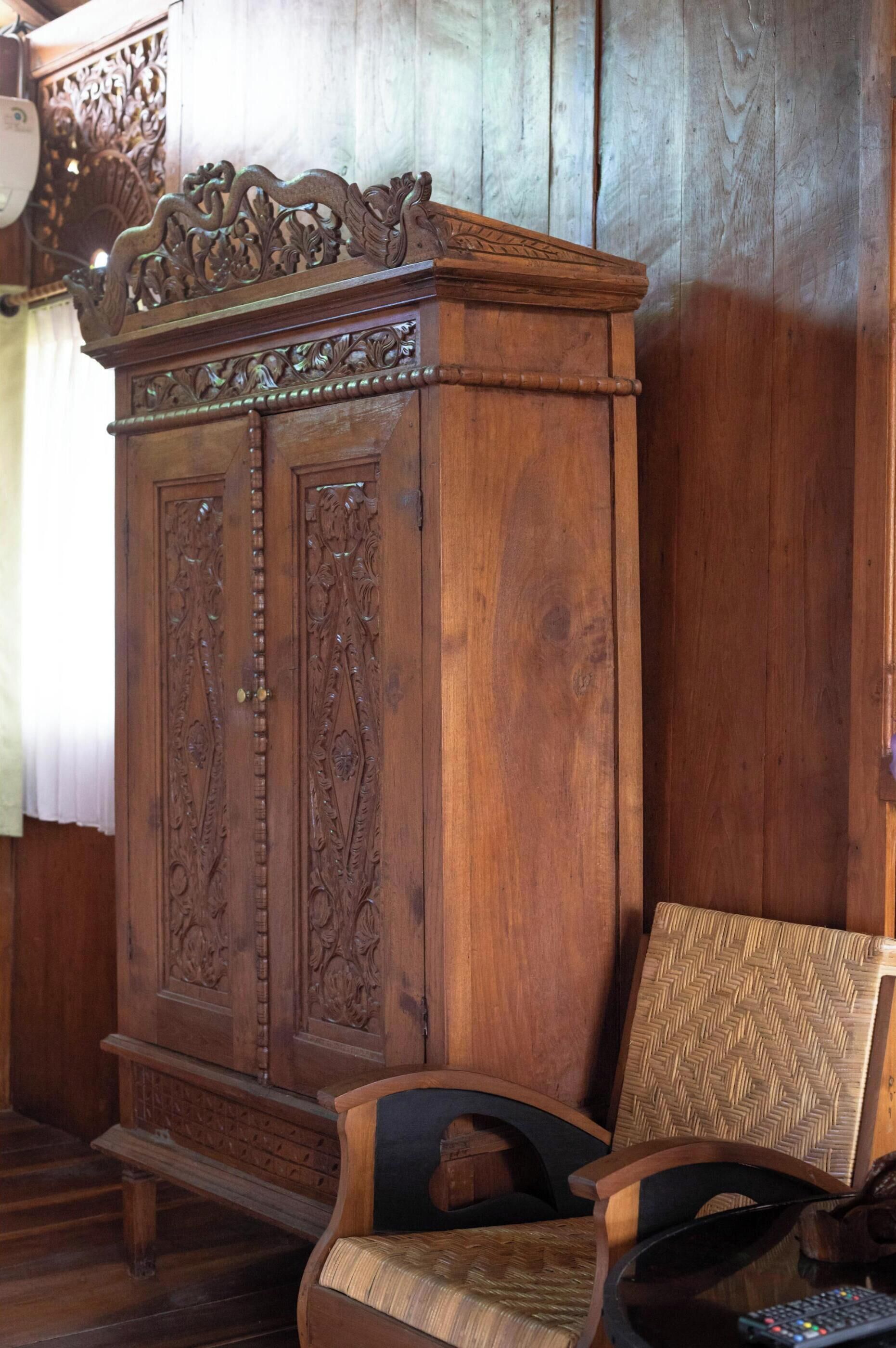 Een houten kast met ingewikkelde houtsnijwerken, een stoel met een geweven zitvlak, en een houten wand.
