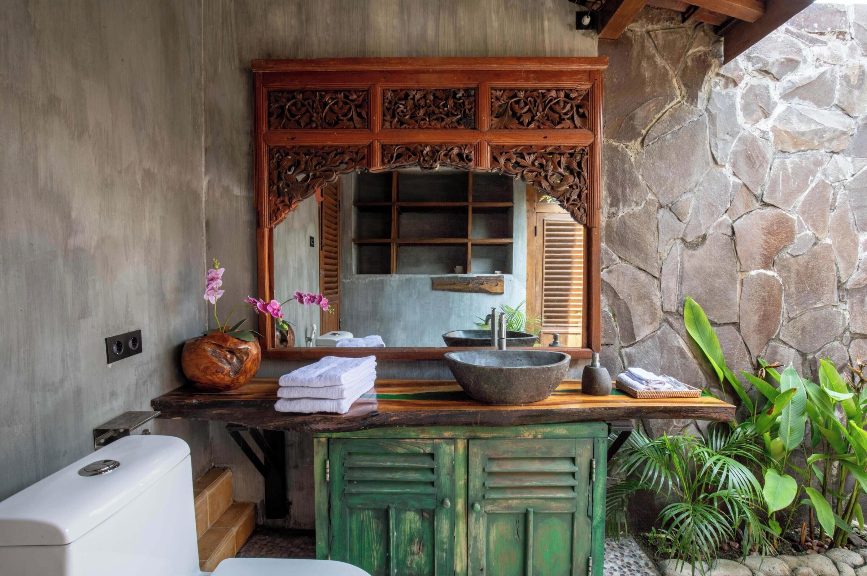 A bathroom with a stone wall, a wooden vanity, a large mirror, and a sink with a stone basin.