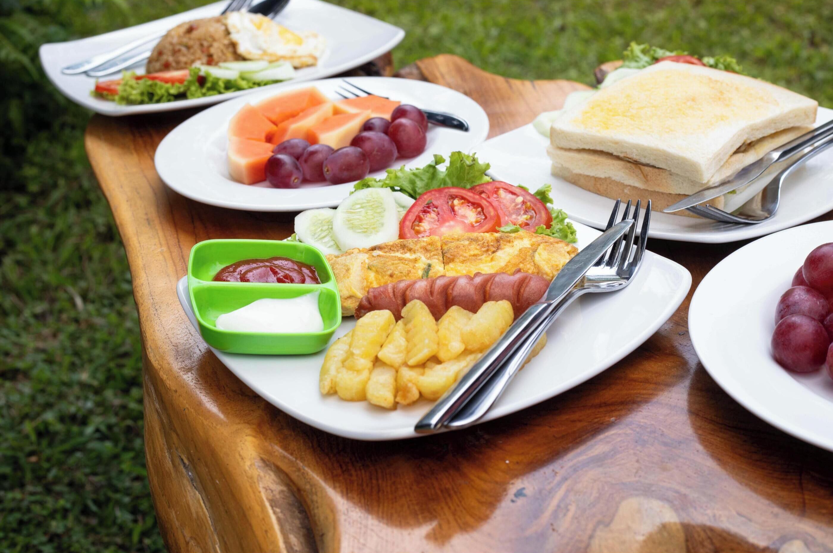 A wooden table with plates of food including a sandwich, salad, and a hot dog.