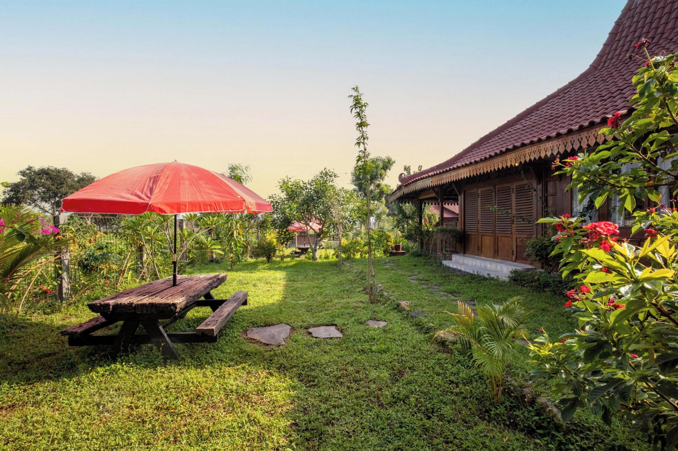 A traditional wooden house with a tiled roof, a red umbrella, and a picnic table in a well-maintained garden.