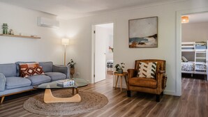 Una sala de estar moderna con un sofá, un sillón y una mesa de centro. Hay un cuadro en la pared y una puerta que da a otra habitación.