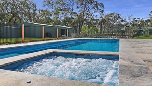 Piscina con zona de jacuzzi, rodeada por un patio cercado y árboles.